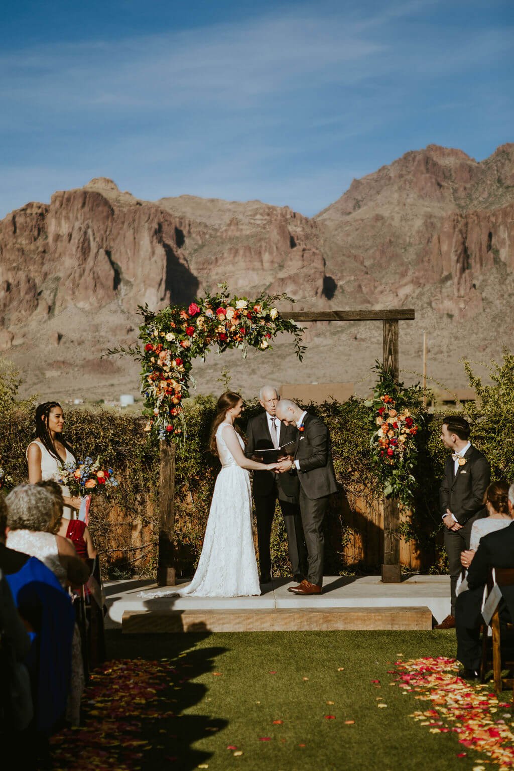 Bride and groom standing under arbor with mountains in the background at Arizona desert wedding
