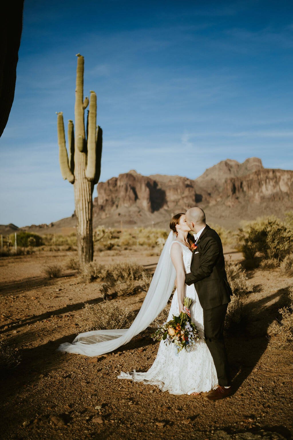 Bride and groom kissing in the desert with cactus in the background