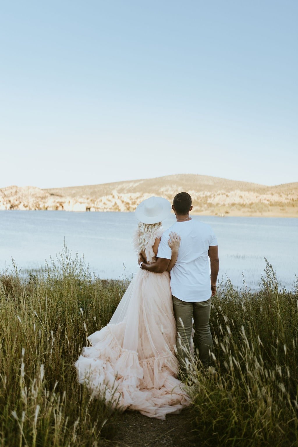 Couple standing in the grass looking out at the lake during engagement photos in Prescott