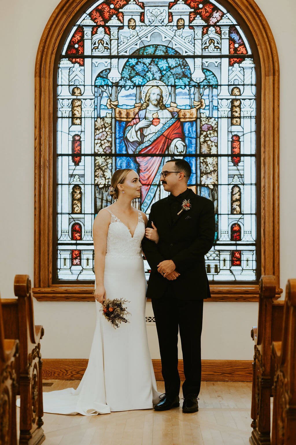 Bride and groom standing in front of stained glass at an intimate chapel wedding