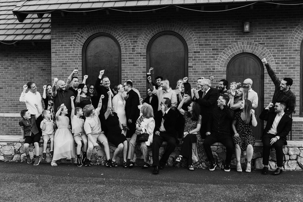 Black and white photo of bride and groom with family and friends at intimate woodland wedding