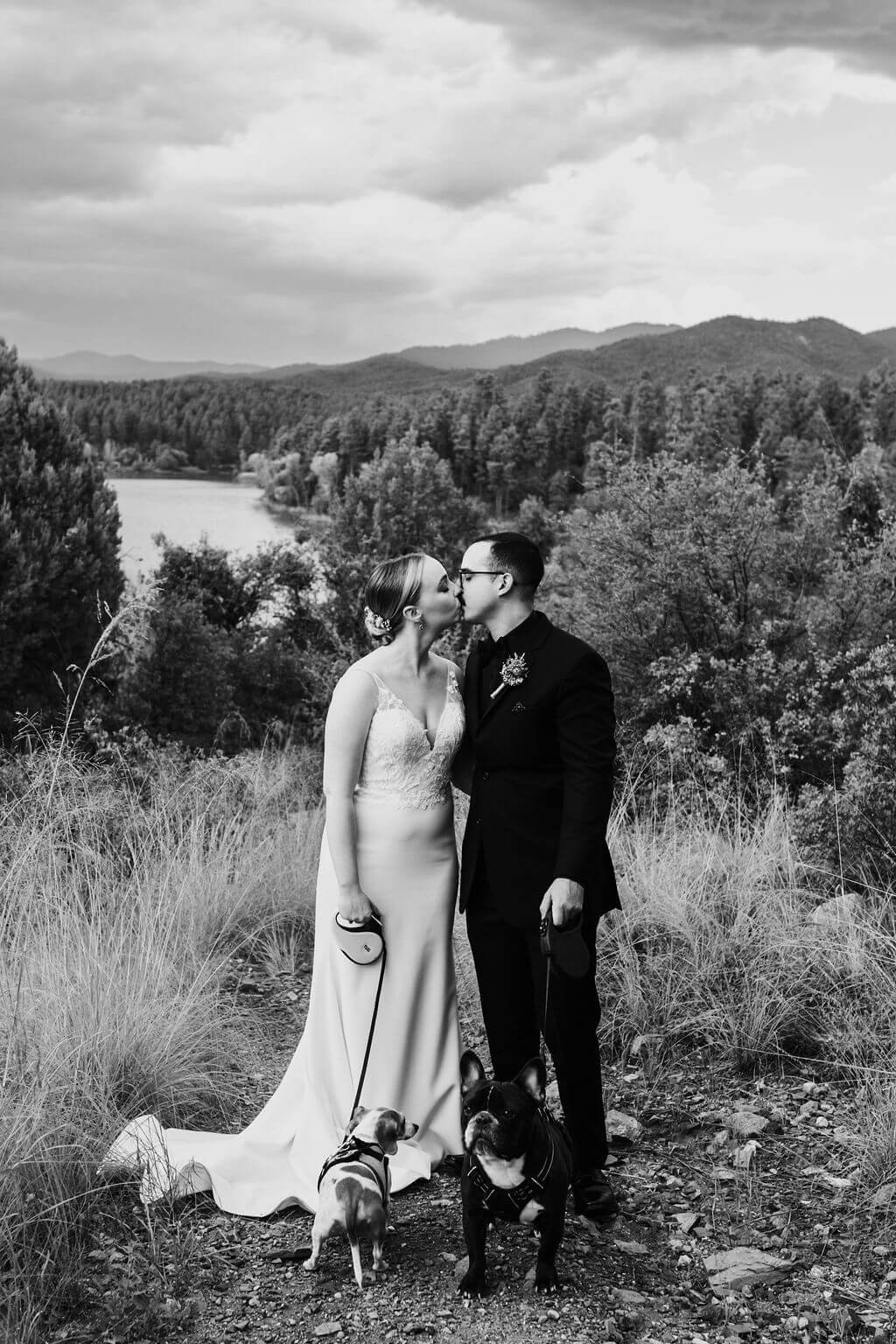 Black and white photo of bride and groom kissing in the woods with lake in the background