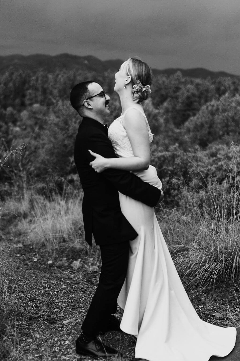 Black and white photo of groom holding bride outside at a woodland wedding