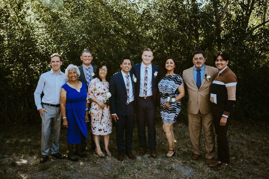 Grooms posing with their family in backyard Southern California wedding