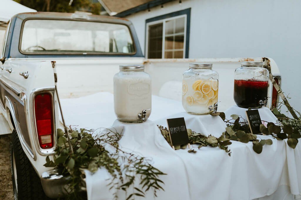 Pick up truck decorated with eucalyptus and flowers with beverages served from the back for Southern California wedding reception