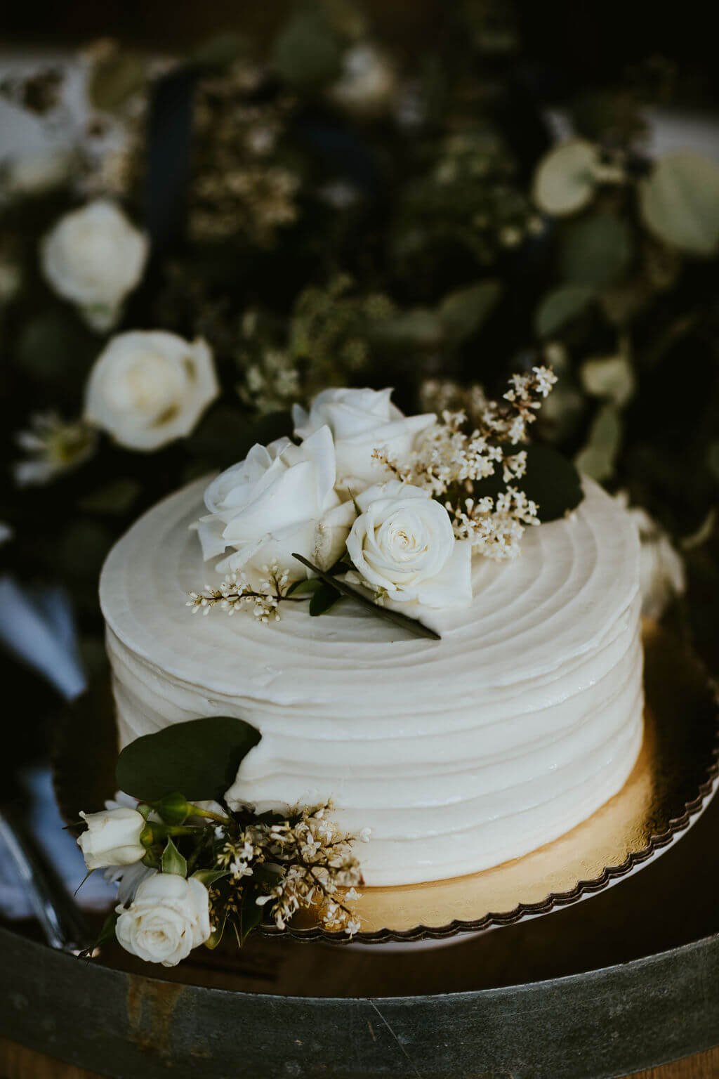 Simple white wedding cake decorated with white roses and dark greens