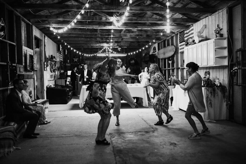 Black and white photo of wedding guests dancing under strung lights in barn at Southern California wedding