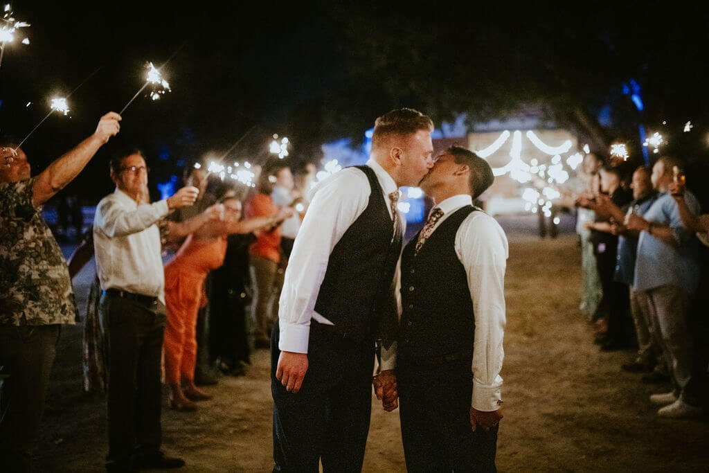 Groom and groom kissing with guests holding sparklers for Southern California wedding send off