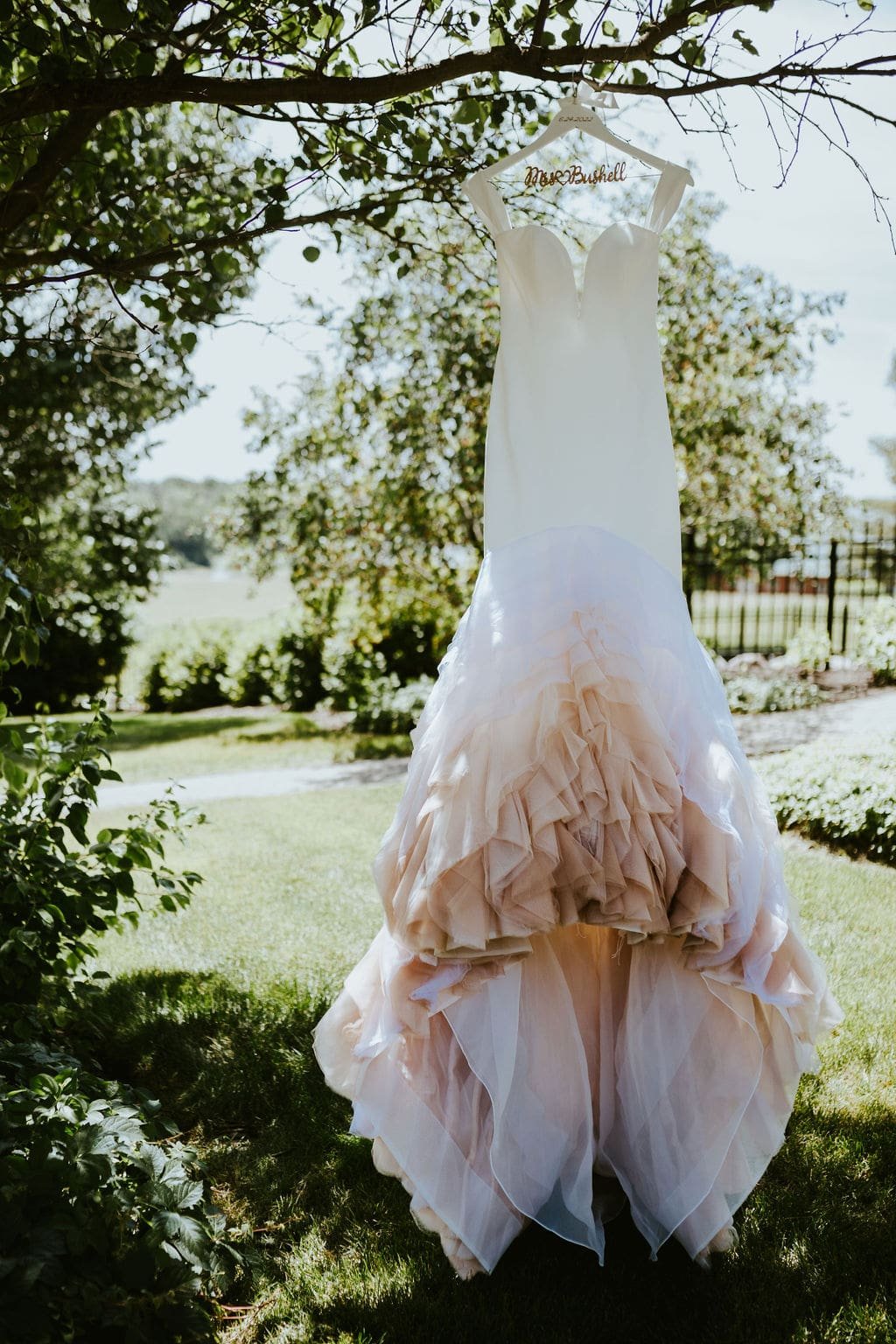 White wedding dress with ombre pink train hanging from a tree at Orchard Ridge Farms