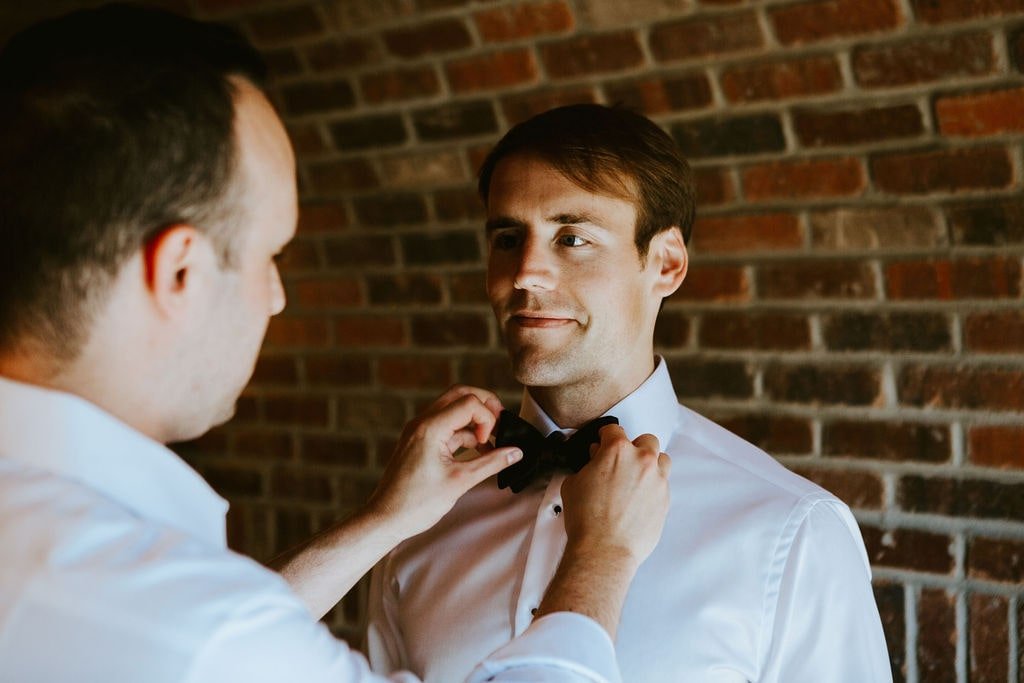 Groomsman helping groom get ready for classic wedding at Orchard Ridge Farms