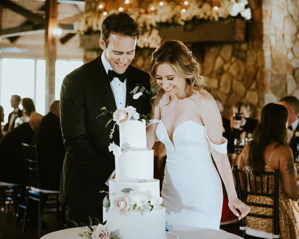 Bride and groom cut their four tier white frosted wedding cake at their classic farmhouse wedding reception