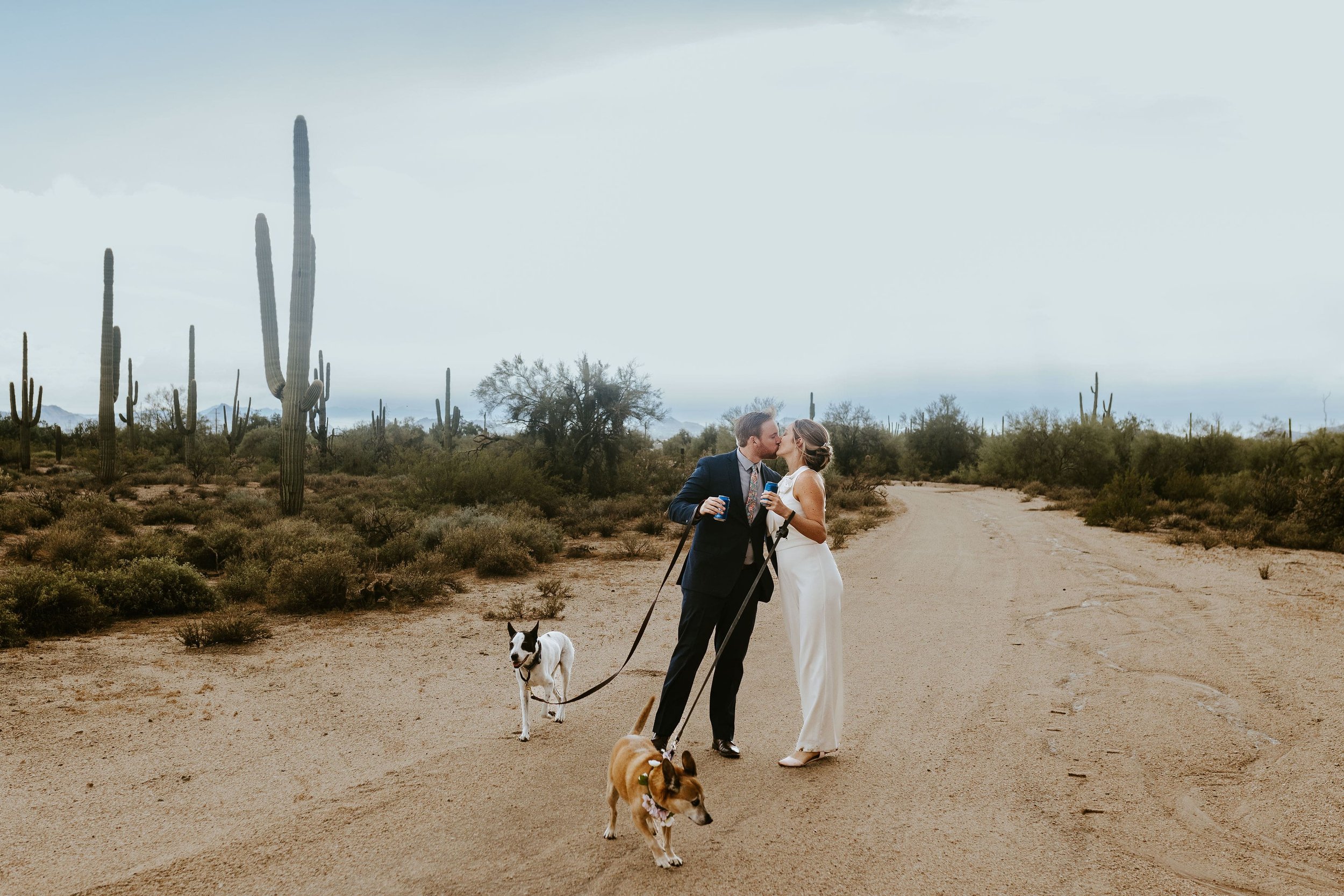 Bride and groom kiss while walking their dogs at their fall desert foothills wedding