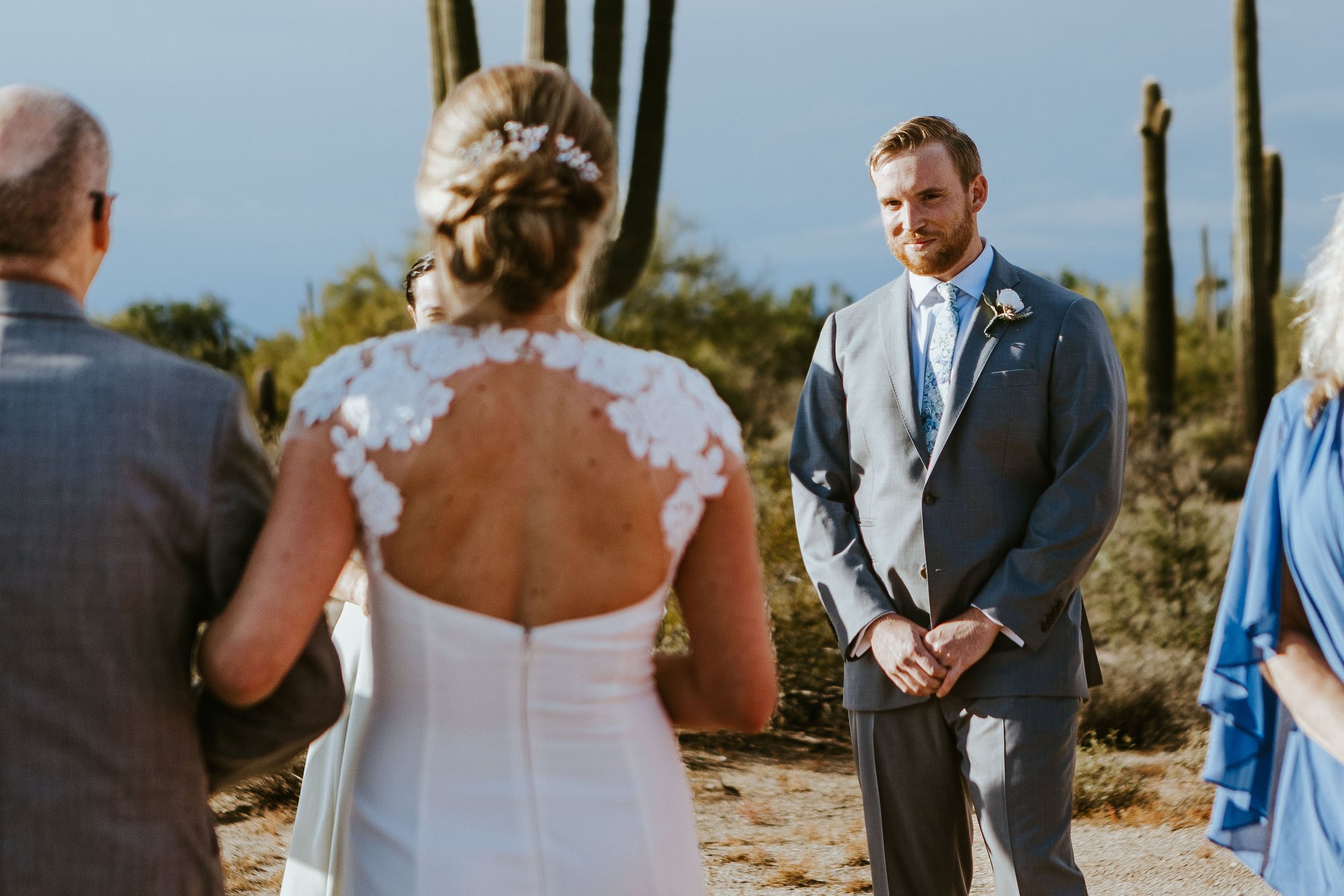 Groom smiles as bride walks down the aisle at their outdoor fall wedding ceremony in Arizona