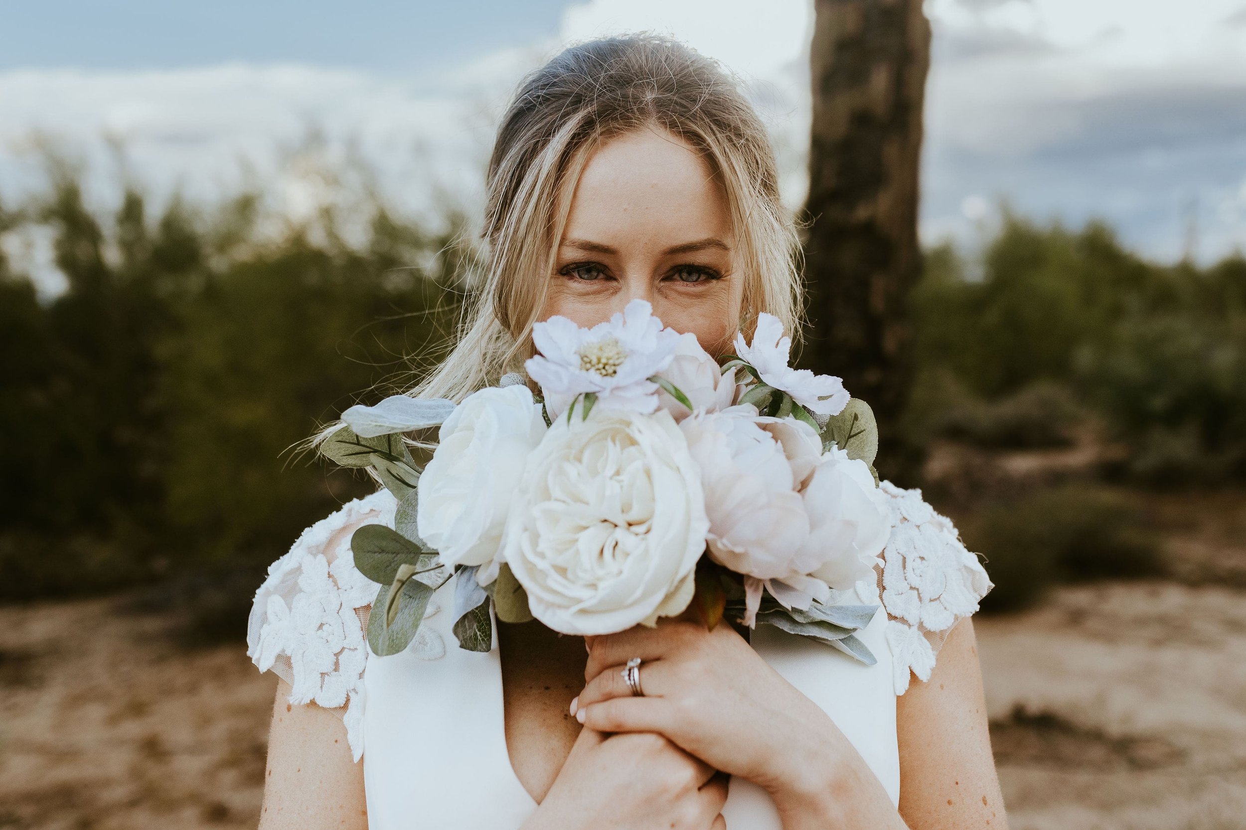 Bride sniffs large bouquet of white wedding flowers 