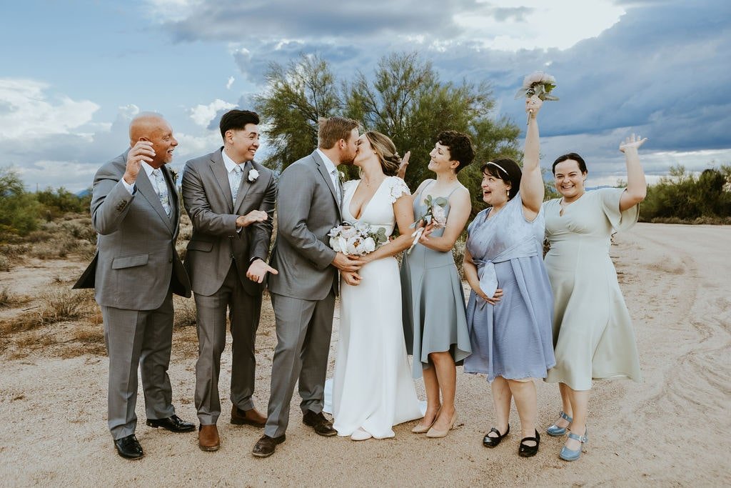 Bride and groom kiss while wedding party looks on
