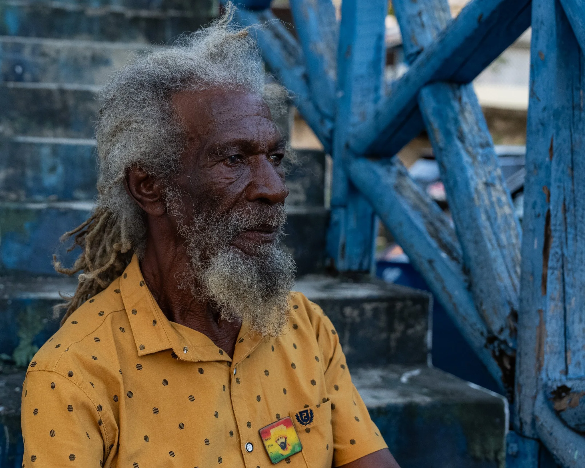 Orlando “Ras Walters” Walters, 1st-generation Rastafari farmer and plant vendor, photographed beside blue wooden stairs in Jamaica.