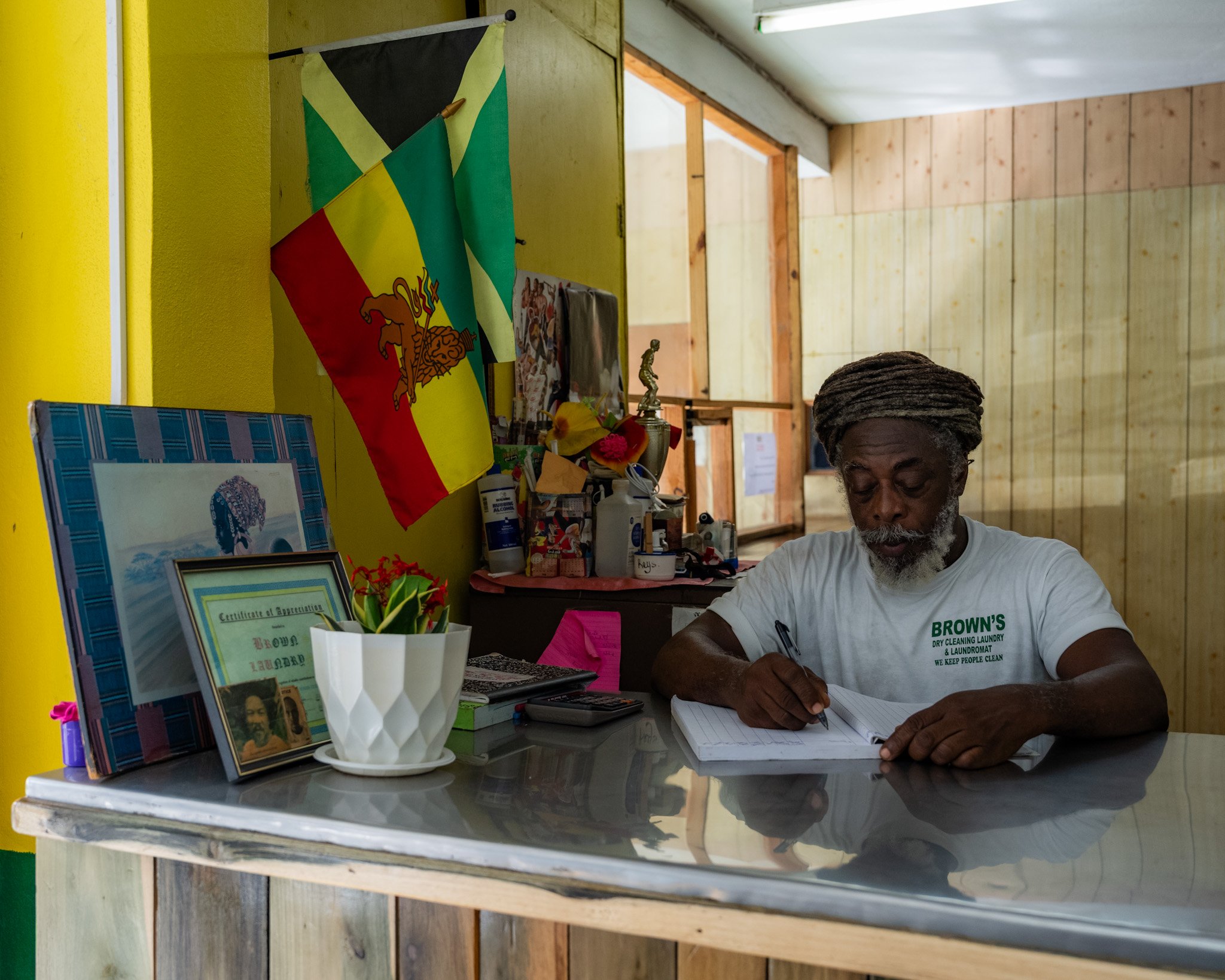 Lewis “Ras Brown” Brown, Rastafari business owner, writing at the counter inside his laundromat and dry-cleaning business in Jamaica.