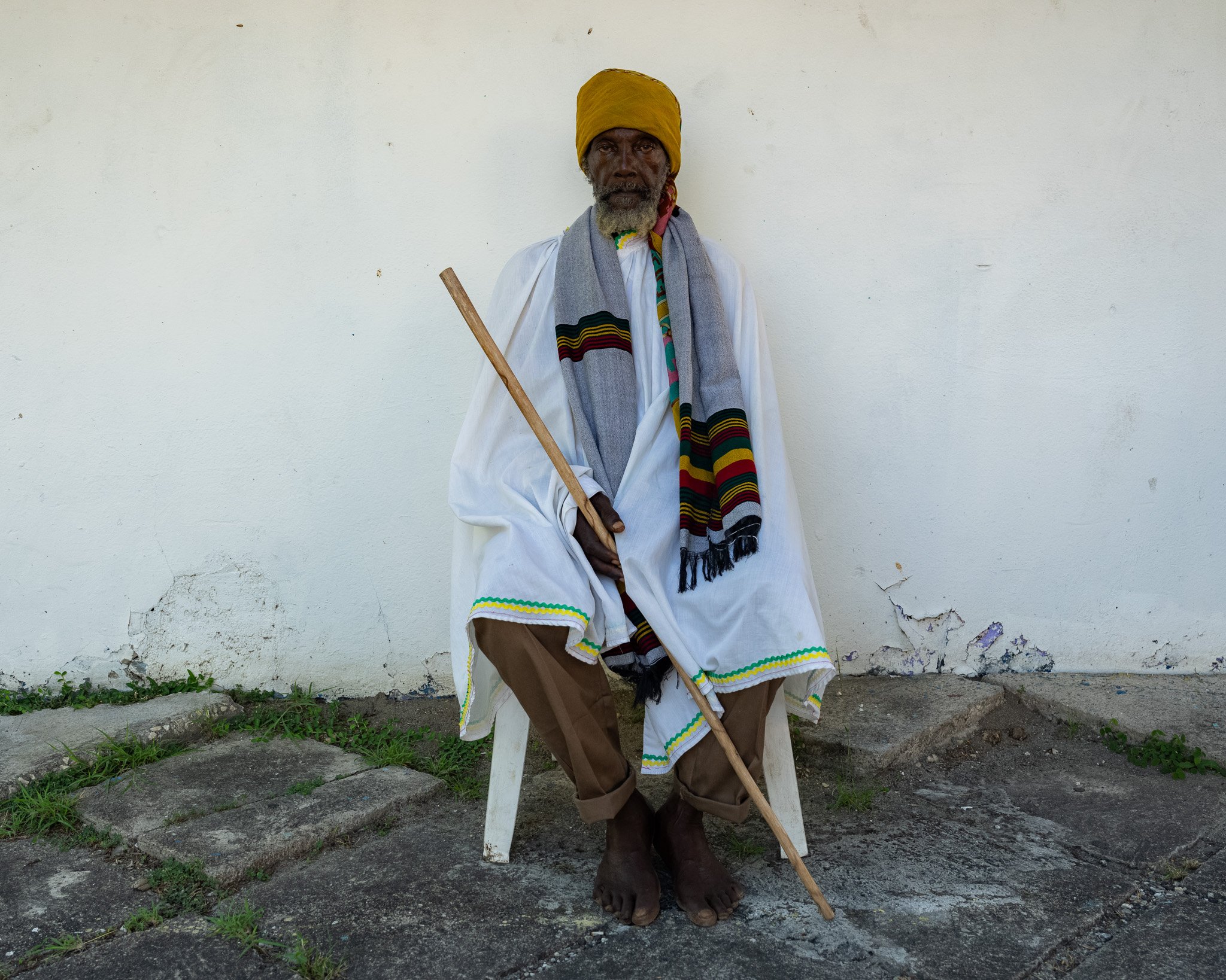 David “Ras IGIE” Elliott, 1st-generation Rastafari holistic healer and artisan, seated in white garments with a staff in Jamaica.