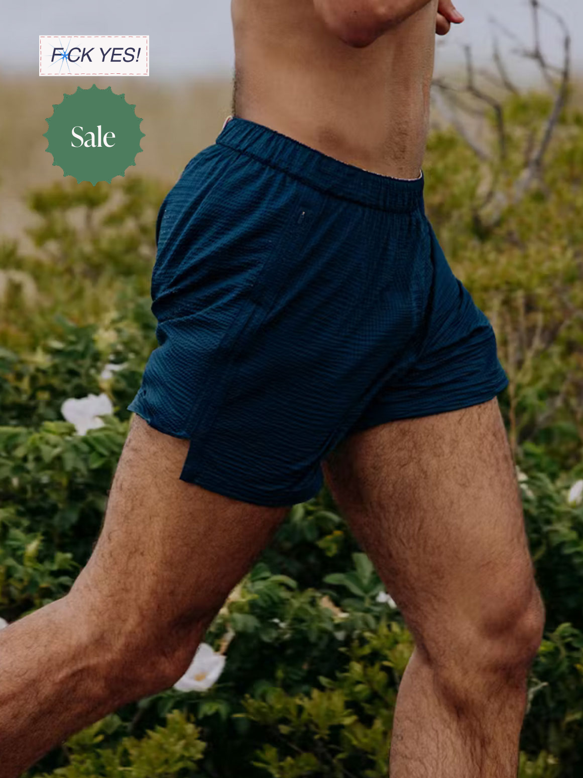 A close-up of a man running outdoors, wearing blue athletic shorts, with greenery and white flowers in the background.