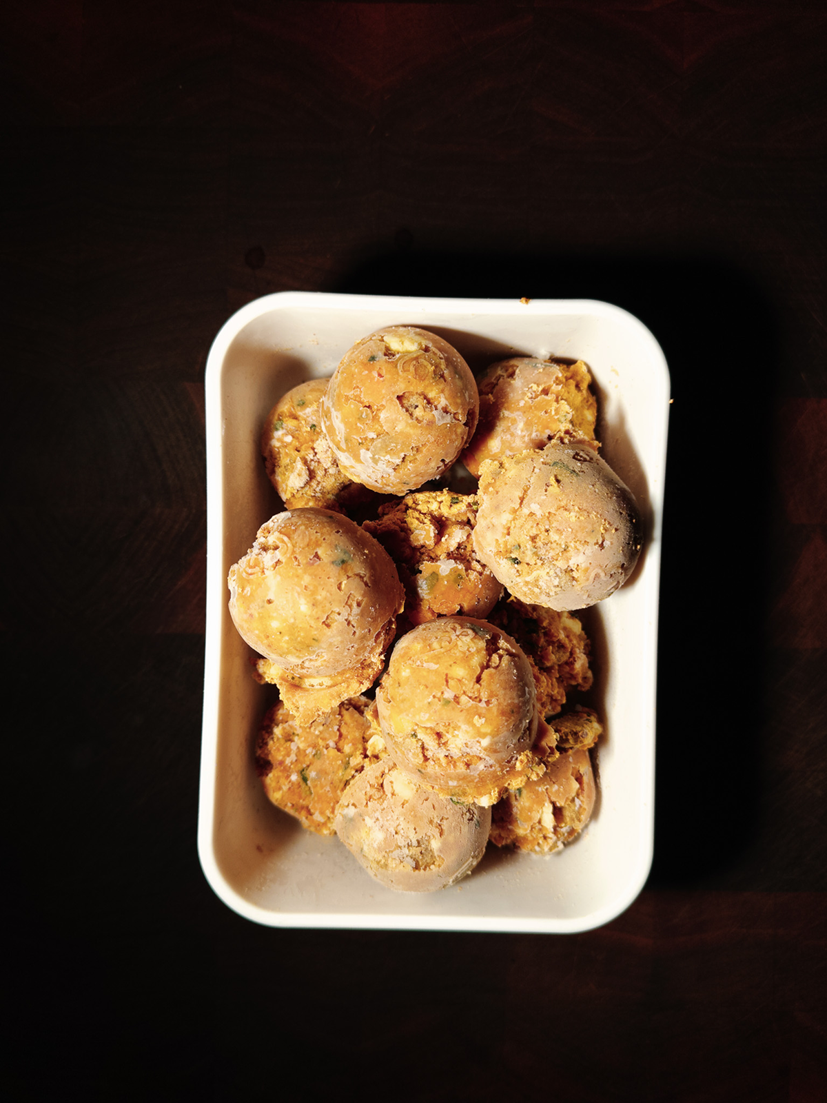 A white container filled with raw, seasoned potatoes on a dark wooden surface.