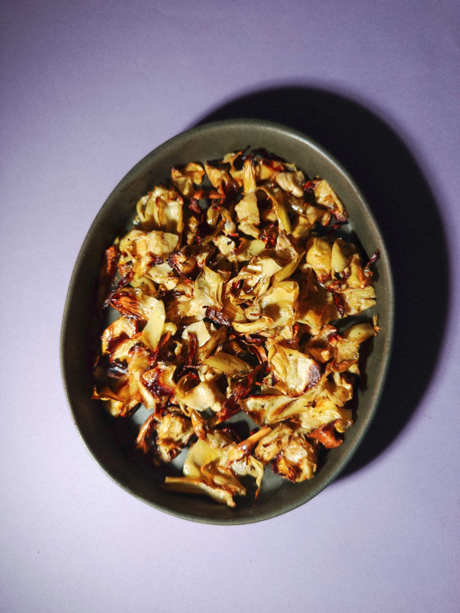 Bowl of roasted cauliflower with charred edges, placed on a white surface.