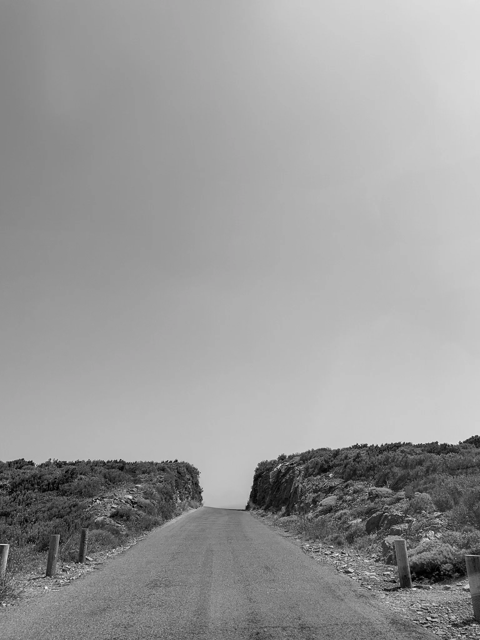 A narrow road with rocks and bushes on both sides, leading to the horizon under a clear sky.