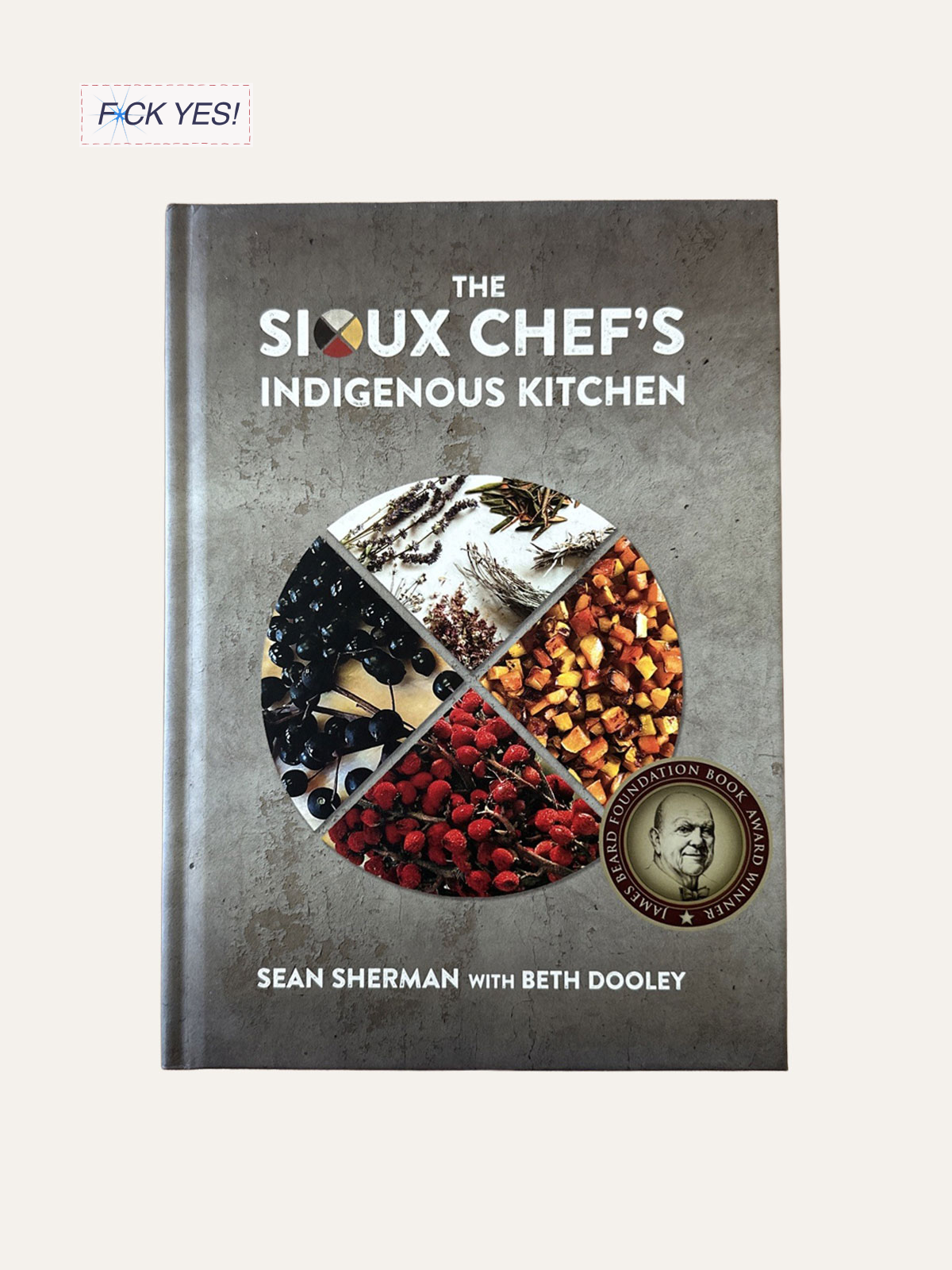 Cover of a cookbook titled "The Sioux Chef's Indigenous Kitchen" by Sean Sherman with Beth Dooley. The cover features a circle divided into four sections, each showing different herbs, spices, and berries.