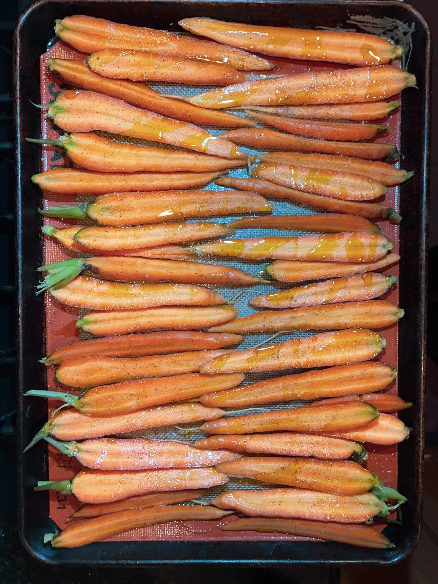 Fresh orange carrots sprinkled with salt or seasoning, arranged on a baking tray lined with a red silicone baking mat.