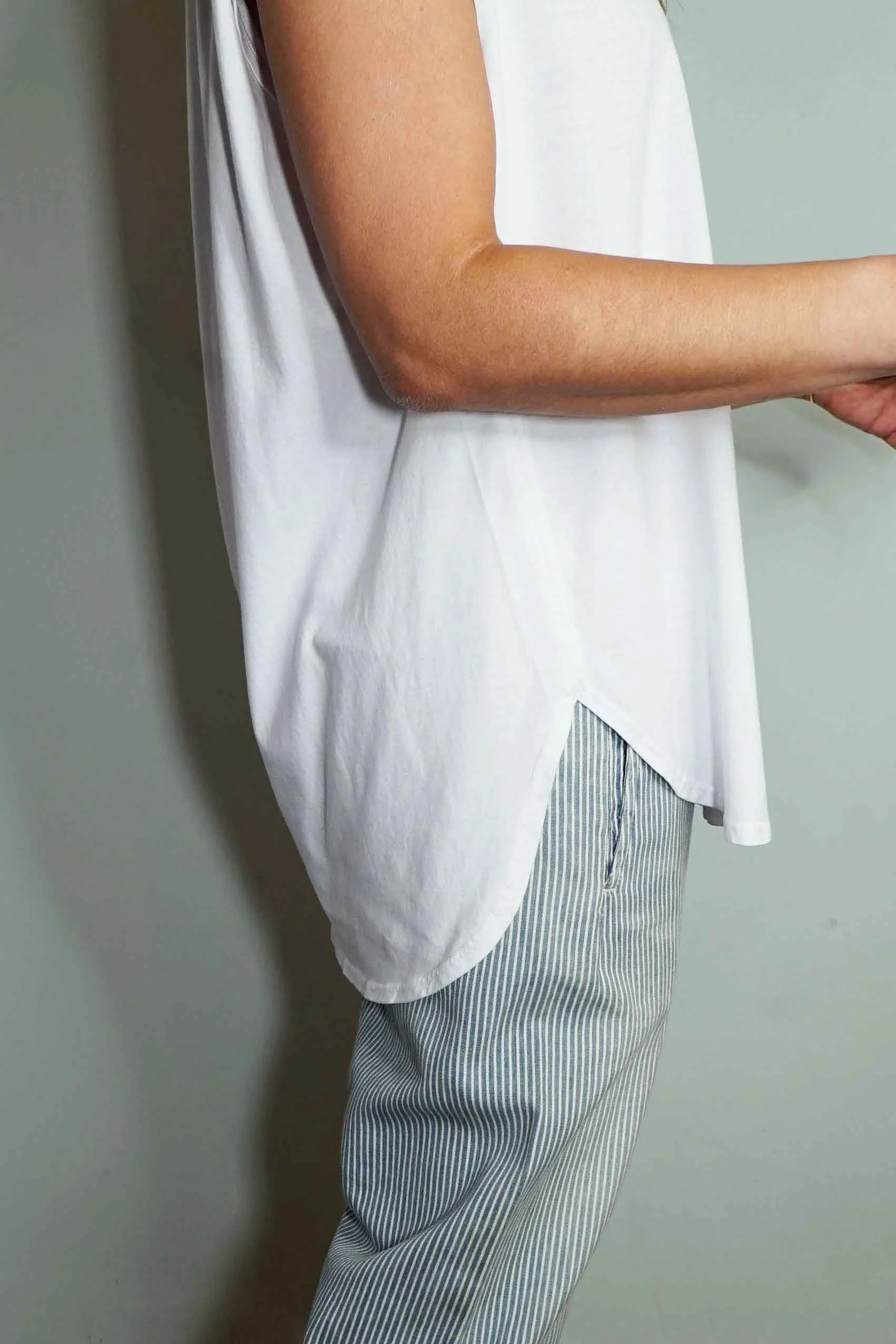 Close-up of a person wearing a loose white top and light-colored striped pants, standing against a plain background.