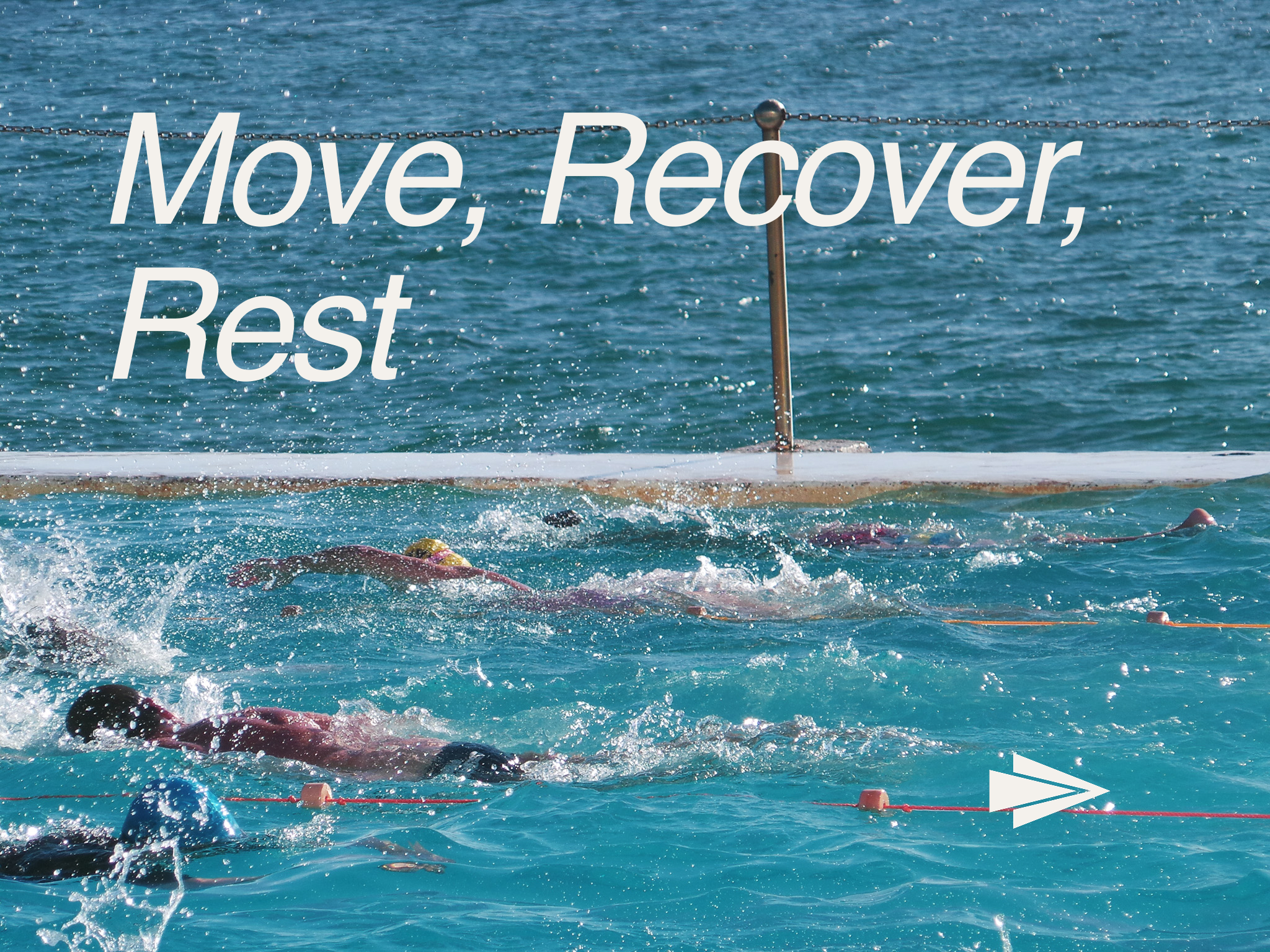 Swimmers competing in an open water race, swimming in blue water marked with orange buoys, with a chain fence in the background and a white arrow at the bottom right.