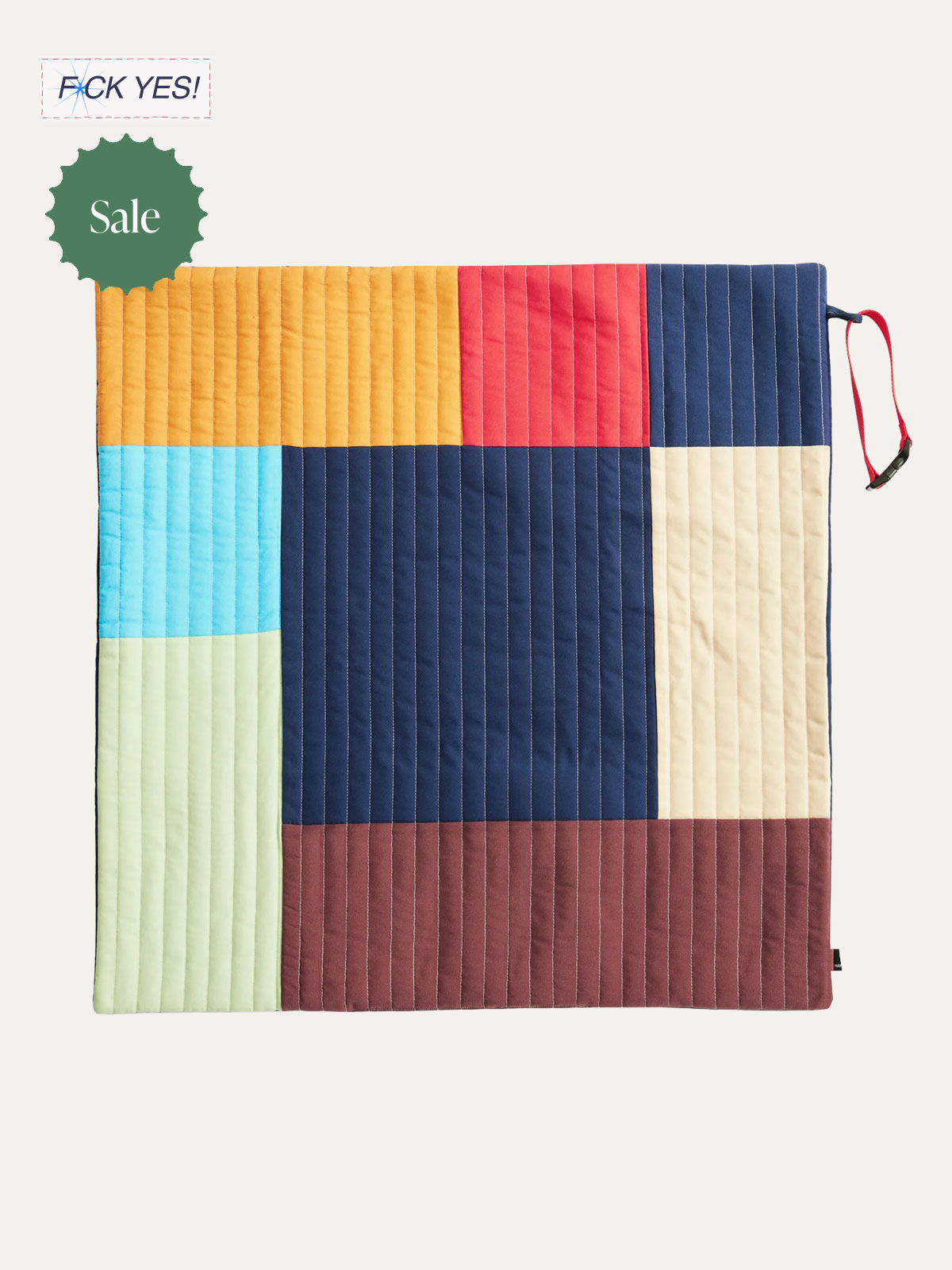 Colorful quilted comforter with blocks in yellow, red, blue, light blue, beige, and brown, with a red strap on the right edge. A green sticker with the word 'Sale' is on the top left corner, and a 'F**K YES!' label is in the top left corner.