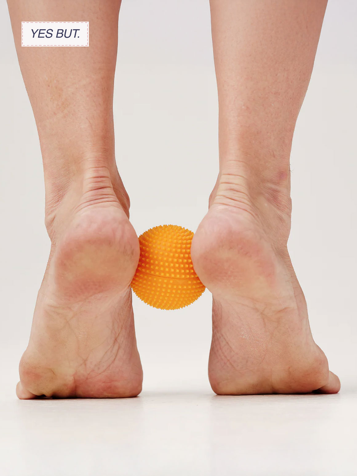 Person standing on their hands with their heels on the ground and a spiky orange massage ball between their ankles.