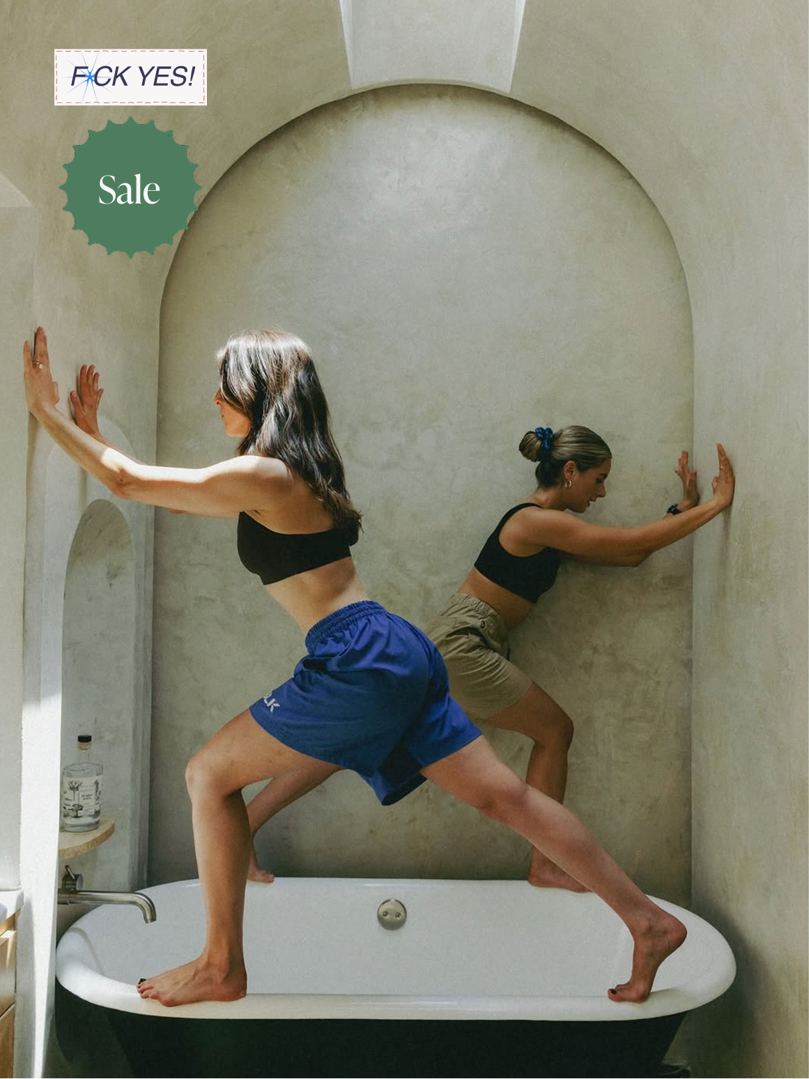 Two women practicing yoga in a bathtub with their hands and feet pressed against the wall, one facing left and the other facing right.