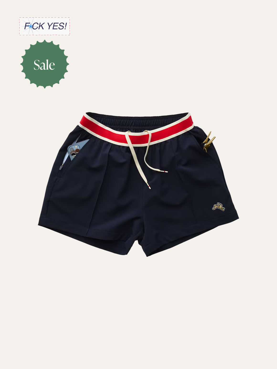 Pair of navy blue shorts with a white and red striped waistband, drawstring tie, a small logo on the bottom right, and a pocket with a phone inside. Two gold items are visible in the pockets.