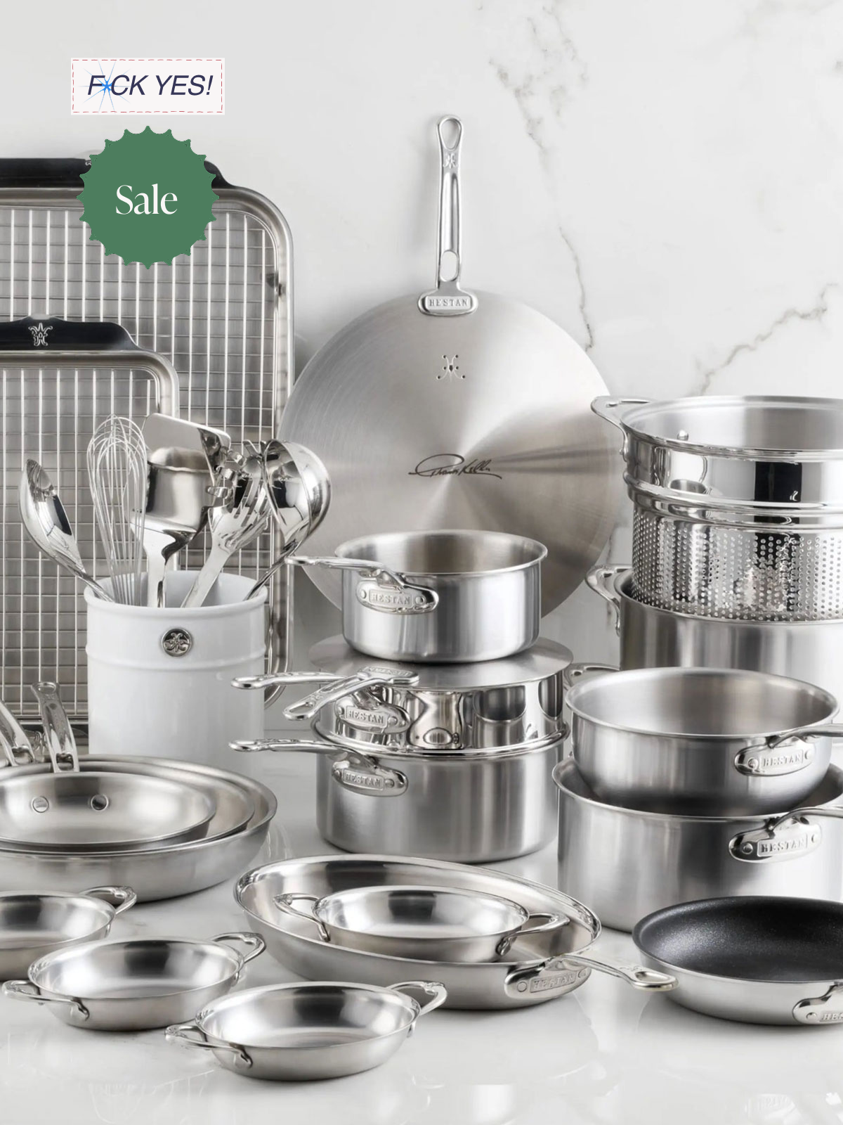 A collection of stainless steel cookware, utensils, and kitchen tools arranged on a white surface with a marble wall background. Includes pots, pans, a colander, a whisk, and a utensil holder.
