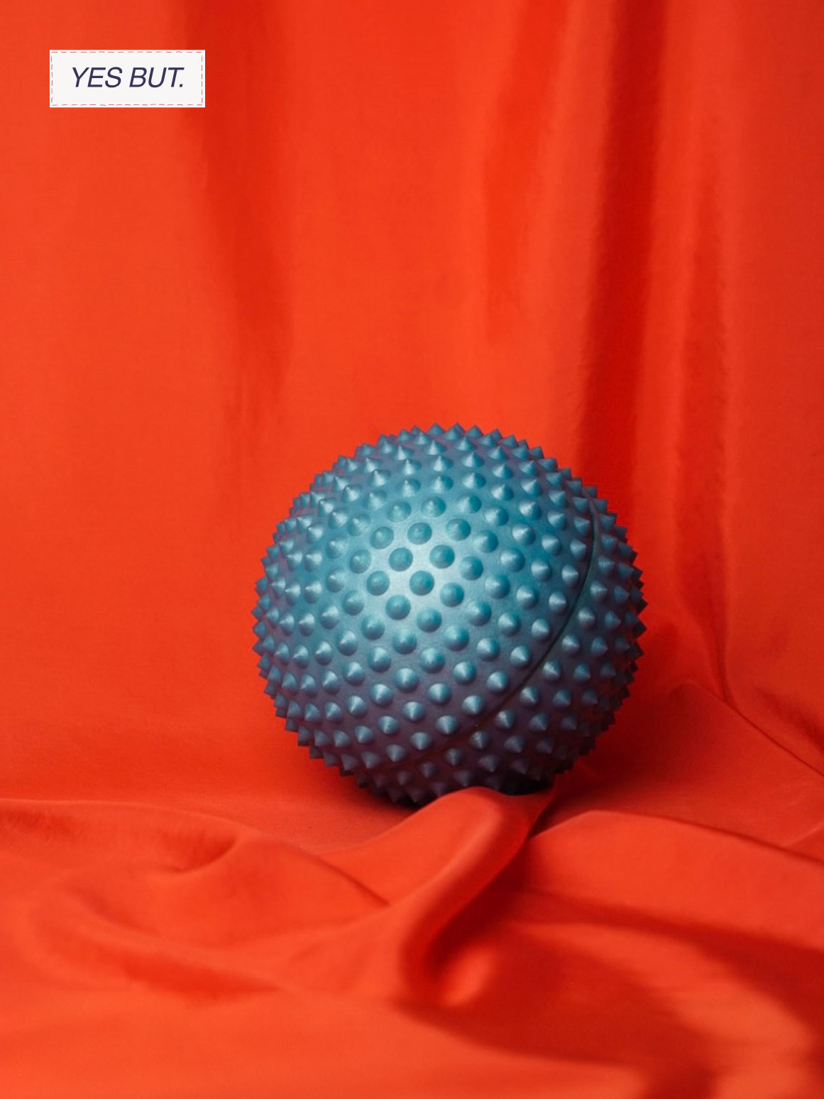 A blue spiky massage ball on an orange fabric background with a label that says "YES BUT."