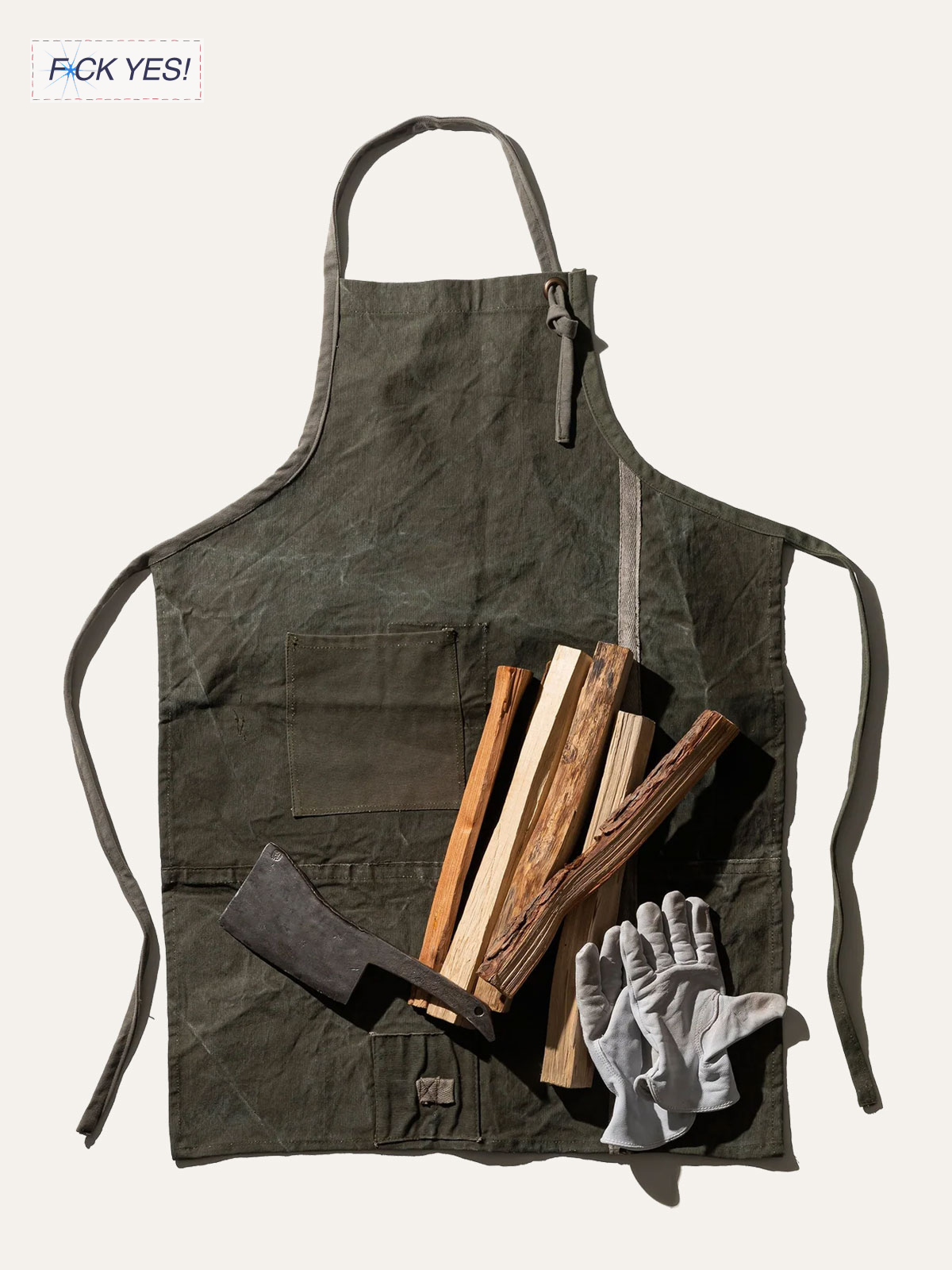 A worn green apron with a front pocket, a white pair of gloves, and several pieces of firewood and kindling on it.