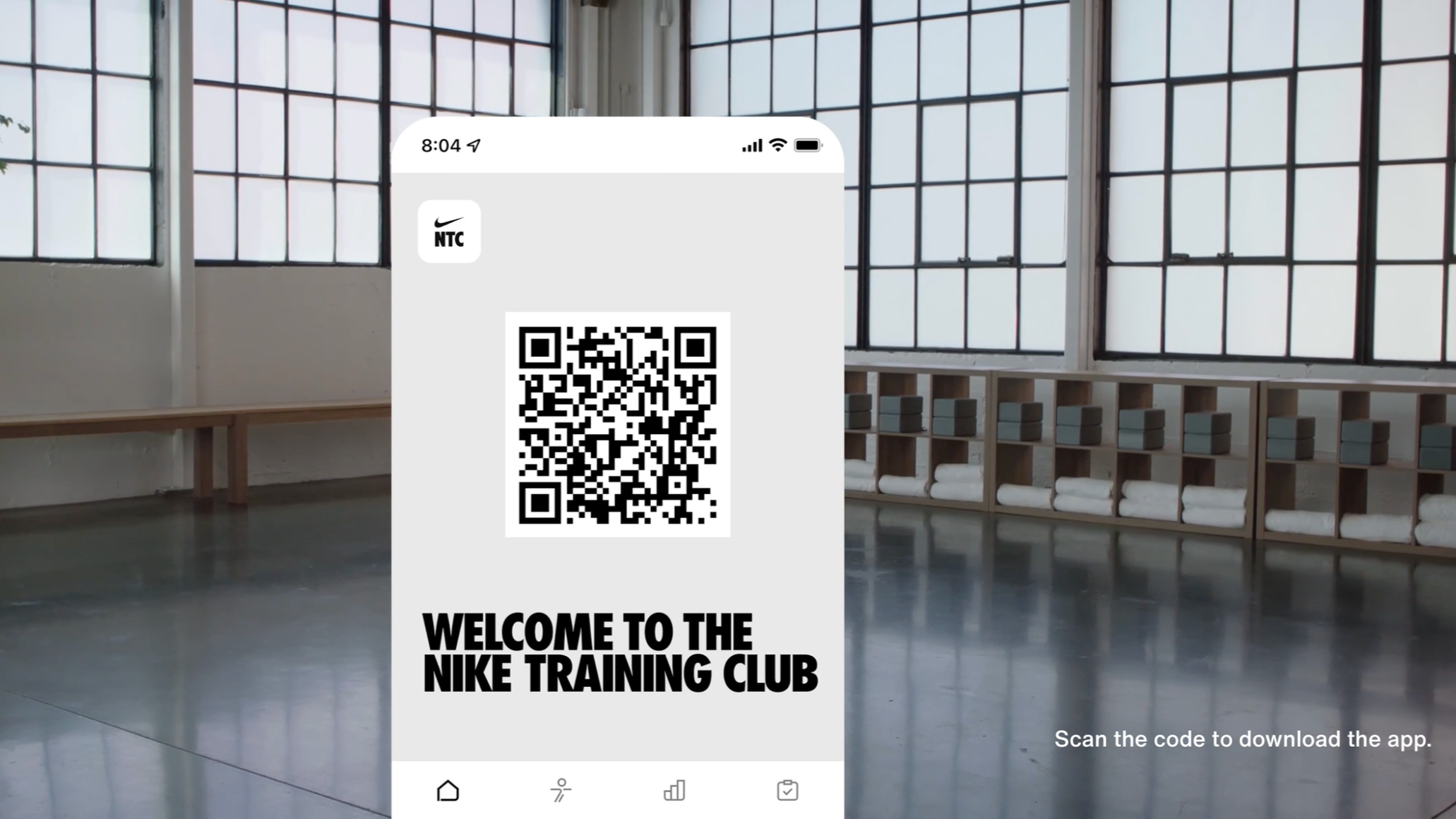A smartphone screen displaying a QR code for the Nike Training Club app, set against a background of a spacious gym with large windows and shelves of towels.