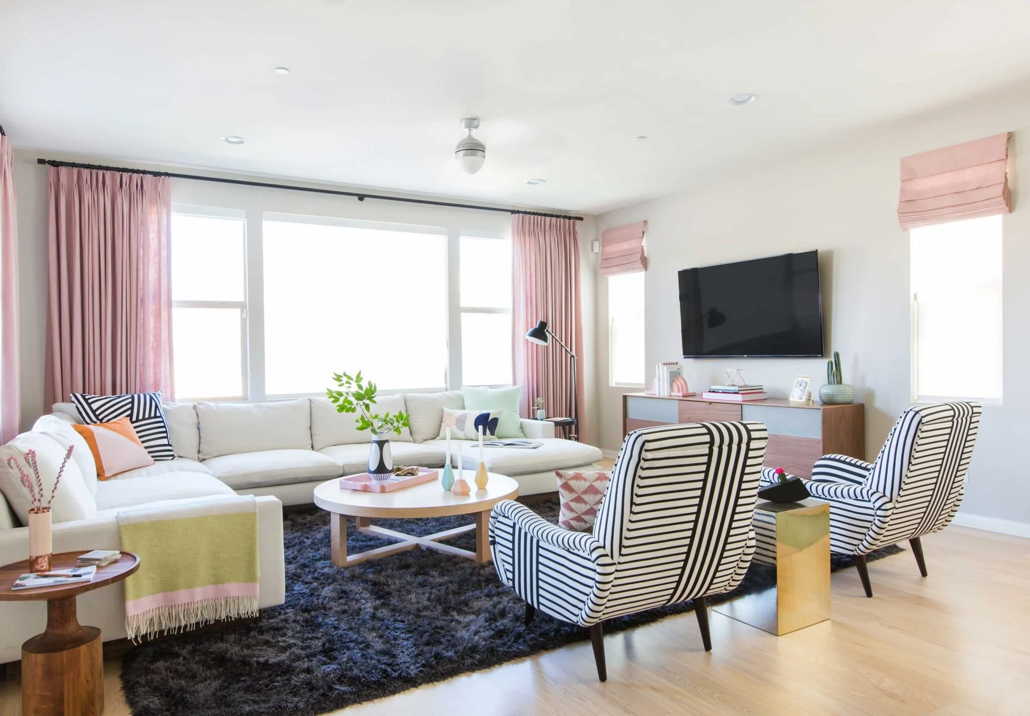 Bright living room with large windows, light sofa, striped chairs, and soft pink curtains creating a fresh spring-inspired space. Design by Emily Henderson