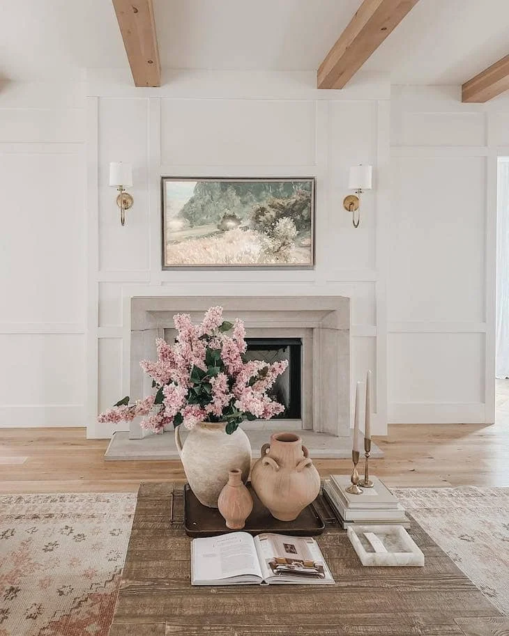 Coffee table styled with a decorative tray holding pottery, candles, books, and pink flowers in a bright living room.