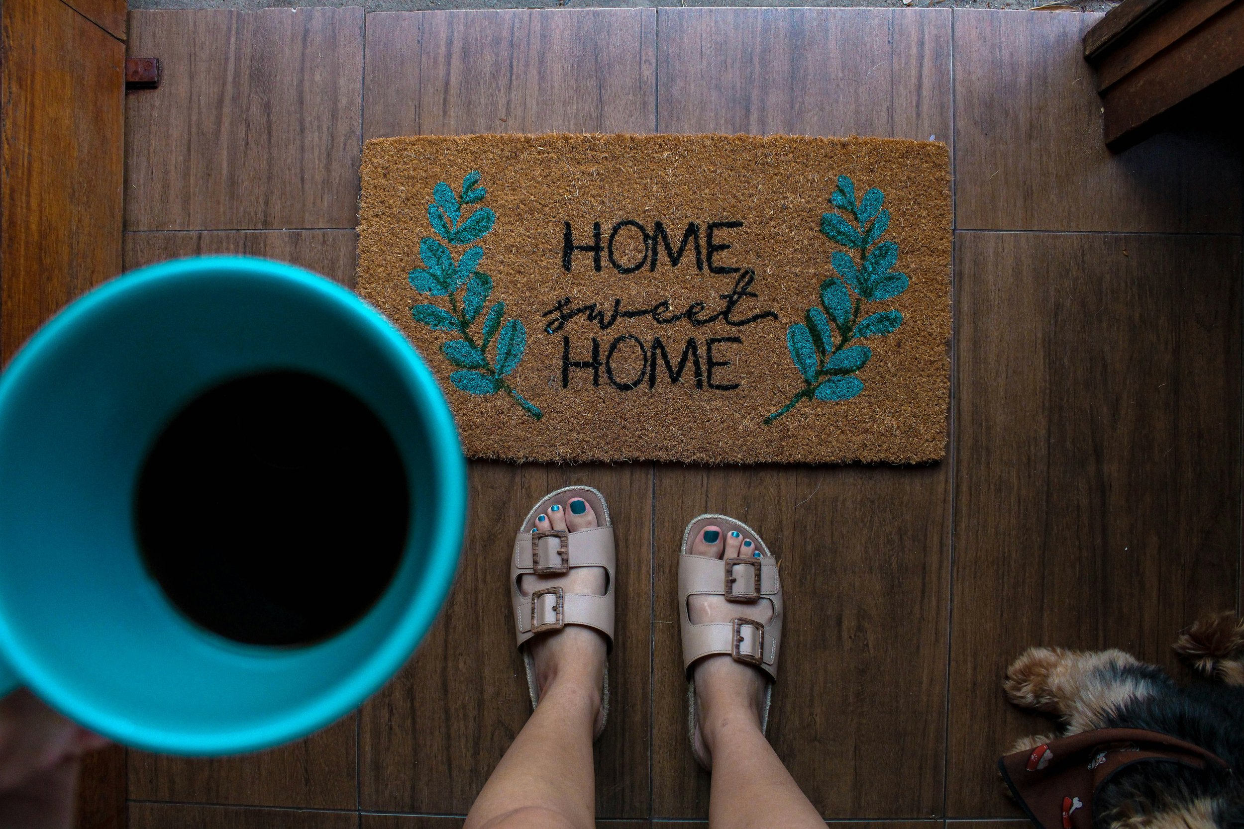 Person standing at a front door with a “home sweet home” doormat and coffee mug, suggesting a welcoming spring entry update.