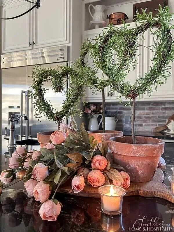 Rosemary heart topiary plants in terracotta pots with pink roses and a candle styled on a kitchen island for simple romantic Valentine’s Day decor.