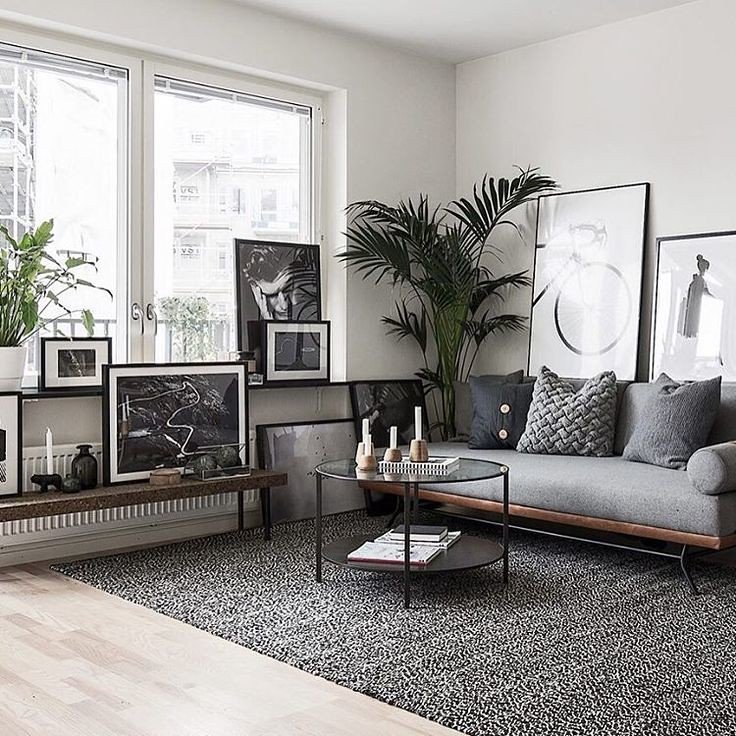 Modern living room with framed artwork leaning along a wall beneath large windows and a gray sofa.
