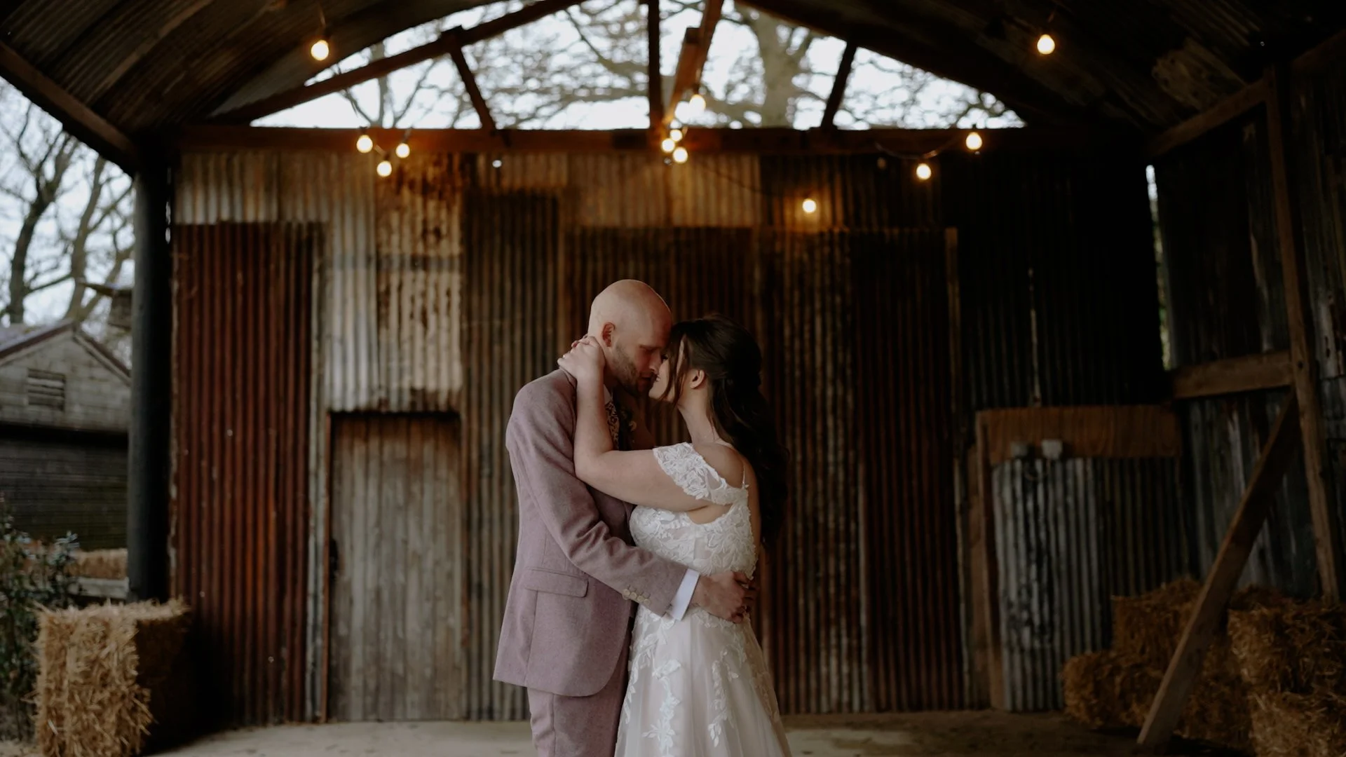 A bride and groom sharing a dance inside a rustic barn with string lights overhead.