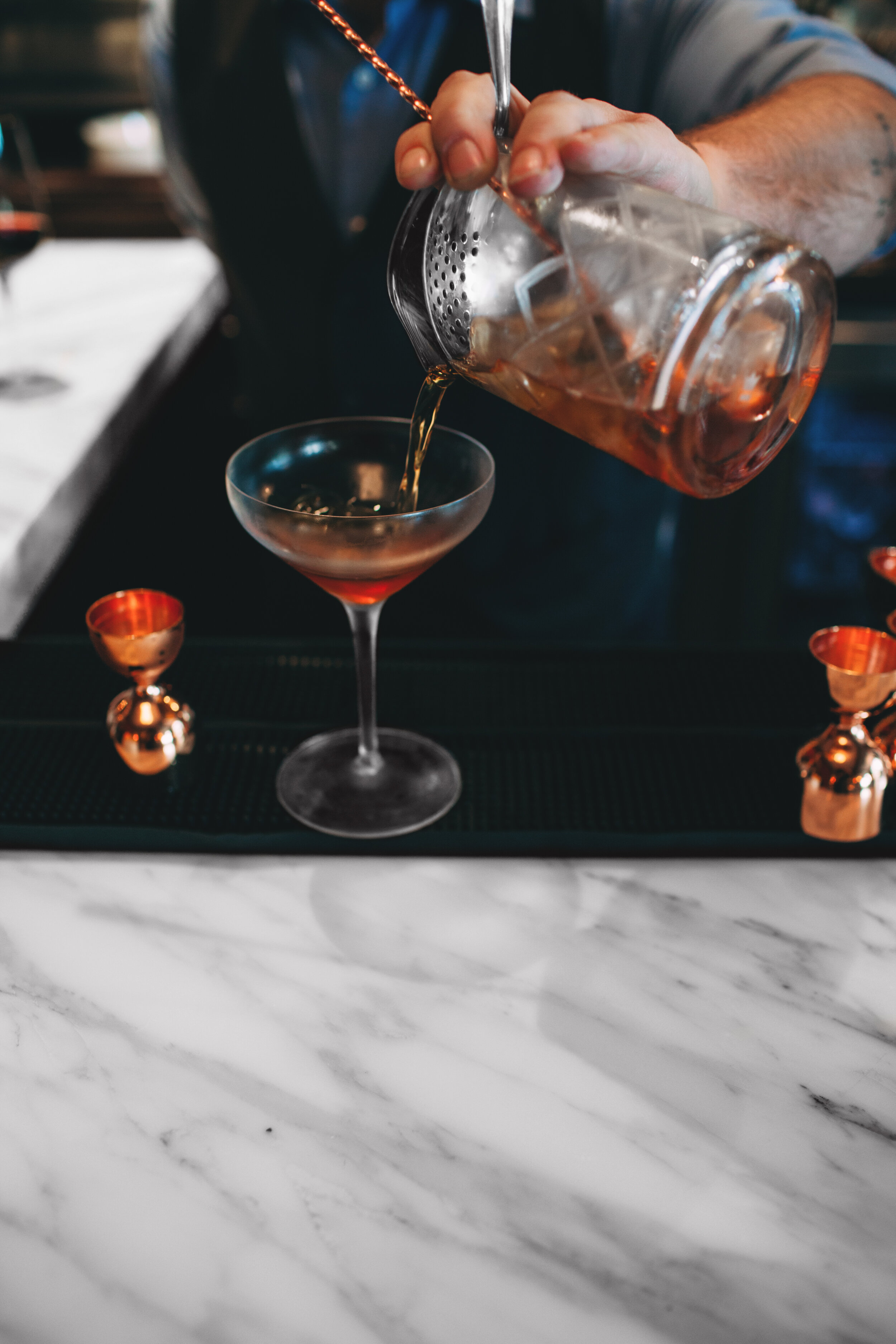  A bartender pouring a meticulously crafted cocktail into a coup glass, showcasing the artistry and attention to detail that goes into our signature drinks 
