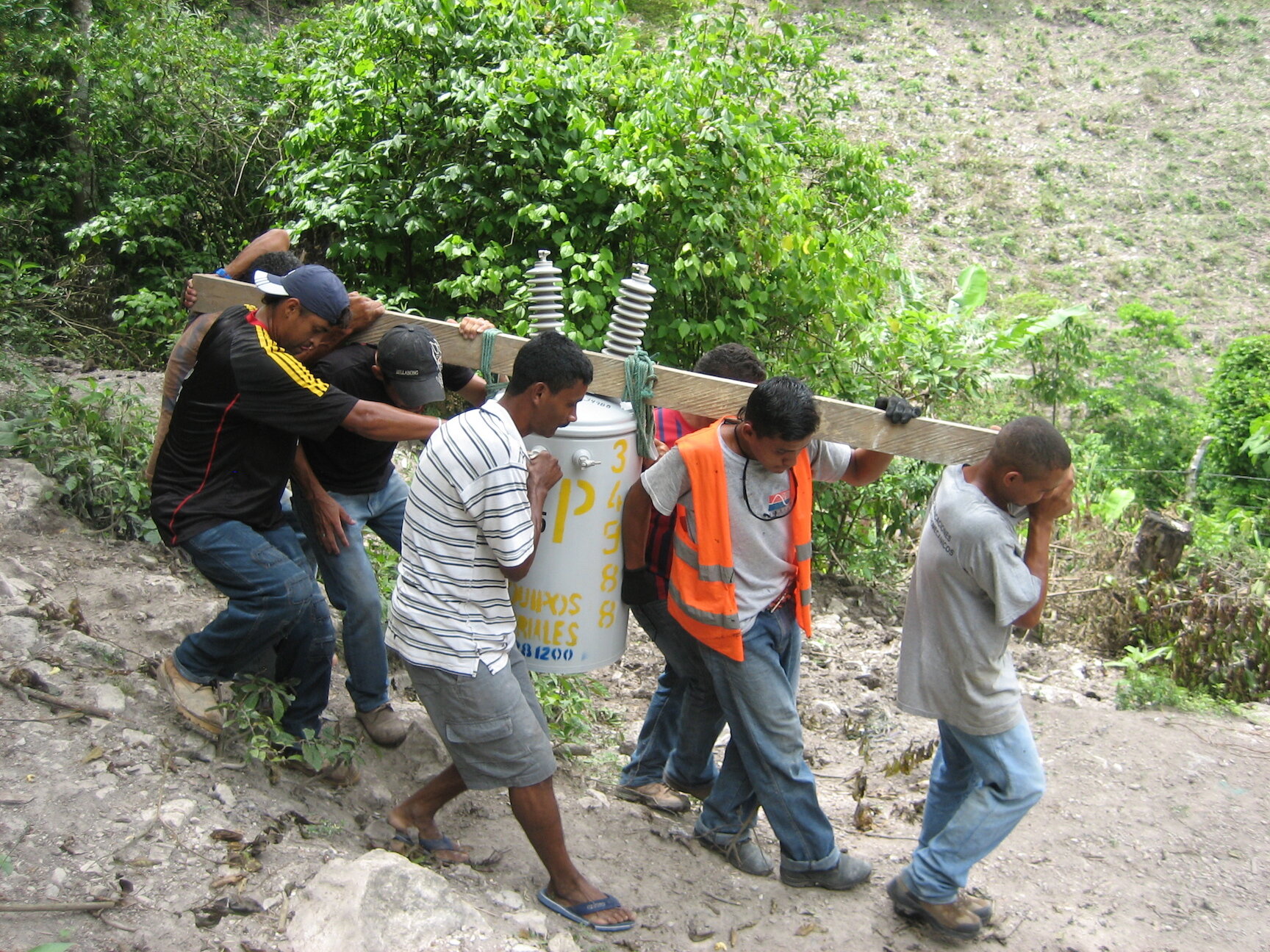 Communiity members team up to carry the electrical transformer to the water source.