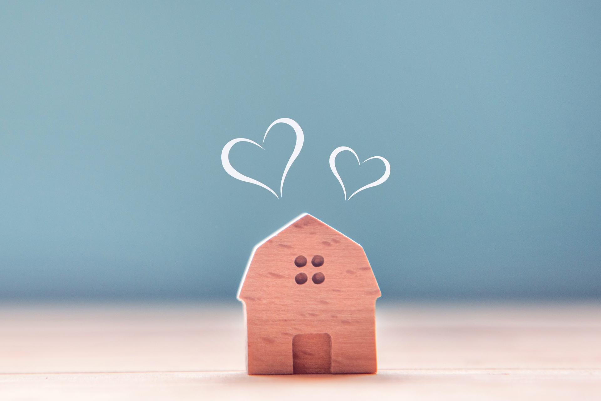 Small wooden house figurine with heart symbols against a light blue background.
