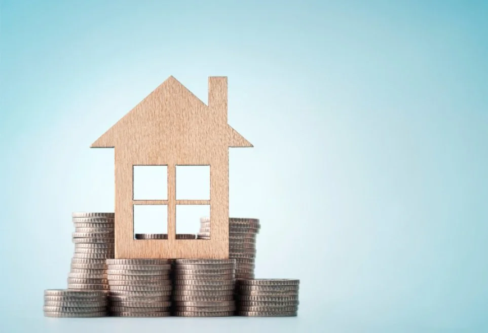 Wooden house model on stacked coins, blue background
