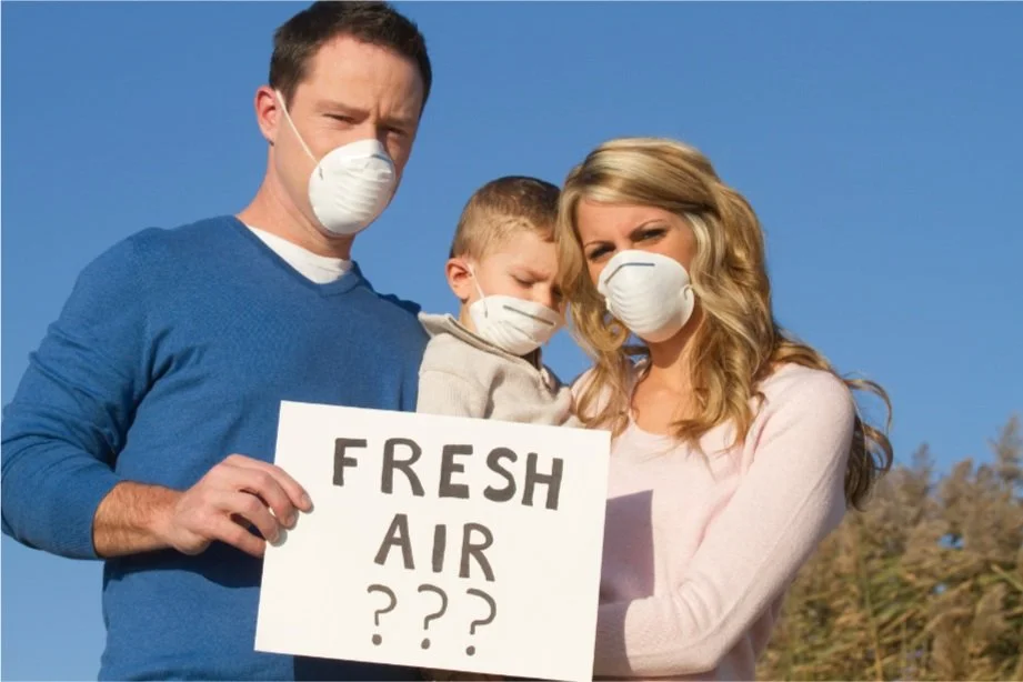 Family wearing masks holding a sign saying "Fresh Air ???" outdoors.