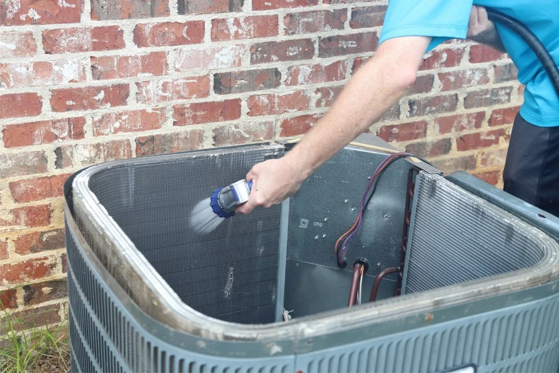 Person cleaning the interior of an air conditioning unit with a hose.